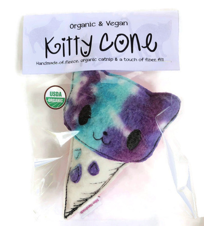 Puede incluir: Un juguete de gato de felpa en forma de cono de helado, con estampado tie-dye morado y azul. El juguete est&aacute; hecho a mano con felpa, hierba gatera org&aacute;nica y relleno de fibra. El juguete tiene una etiqueta USDA Organic.