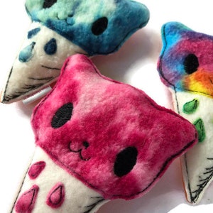 Puede incluir: Tres juguetes de peluche en forma de cono de helado con caras de animales. Los conos son blancos con costuras negras. El helado es rosa, azul y tie-dye arco&iacute;ris.