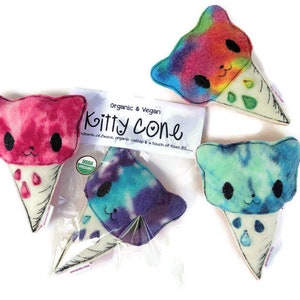 Puede incluir: Tres conos de helado de peluche con forma de gato. Los conos est&aacute;n hechos de fieltro blanco y tienen un patr&oacute;n tie-dye en rosa, azul y verde. Los conos est&aacute;n etiquetados como "Organic & Vegan Kitty Cone" y "USDA Organic".