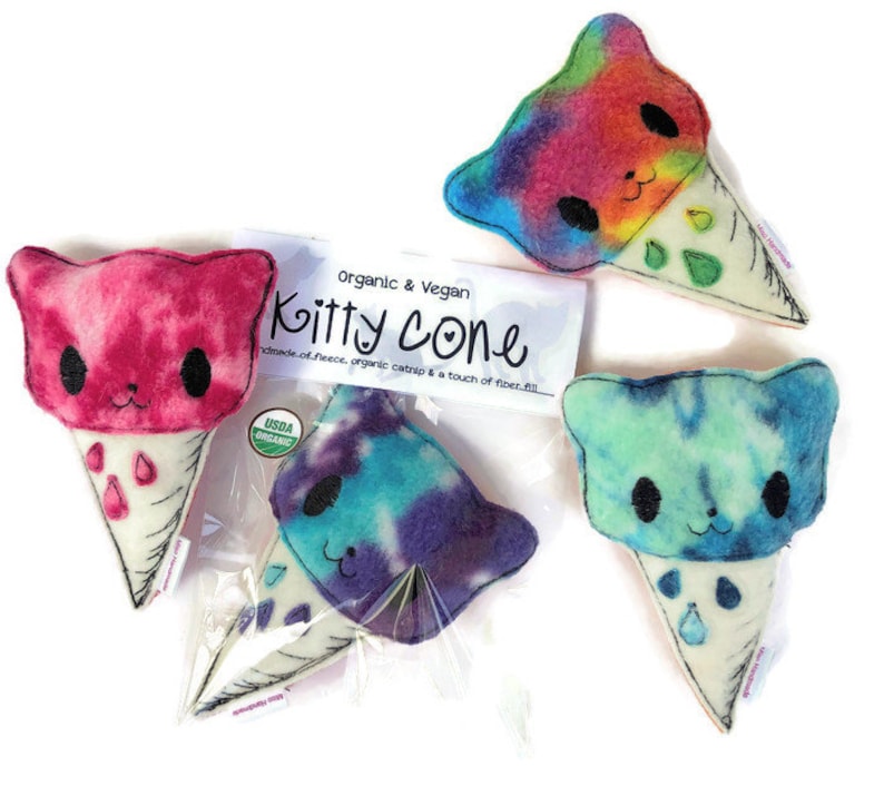 Puede incluir: Tres conos de helado de peluche con forma de gato. Los conos est&aacute;n hechos de fieltro blanco y tienen un patr&oacute;n tie-dye en rosa, azul y verde. Los conos est&aacute;n etiquetados como "Organic & Vegan Kitty Cone" y "USDA Organic".