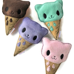 Puede incluir: Cuatro juguetes de peluche de cono de helado con gatos. El helado es de color marr&oacute;n, verde, morado y rosa. Cada cono tiene una base marr&oacute;n y un dise&ntilde;o de goteo blanco.