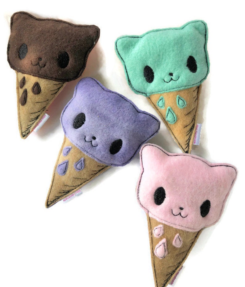 Puede incluir: Cuatro juguetes de peluche de cono de helado con gatos. El helado es de color marr&oacute;n, verde, morado y rosa. Cada cono tiene una base marr&oacute;n y un dise&ntilde;o de goteo blanco.