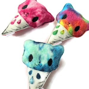Puede incluir: Tres juguetes de peluche en forma de cono de helado con tela de te&ntilde;ido anudado y caras bordadas. Los conos de helado son rosa, azul y arco&iacute;ris.