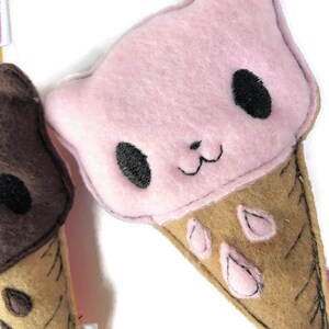 May include: Two felt ice cream cone plushies. One is pink with black eyes and a brown cone. The other is brown with black eyes and a tan cone.
