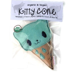 May include: A green felt cat-shaped toy in the form of an ice cream cone. The toy is packaged in a clear plastic bag with a label that reads "Organic & Vegan Kitty Cone Handmade of fleece, organic catnip & a touch of fiber fill" and a USDA Organic seal.