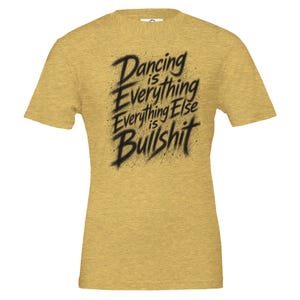 Könnte beinhalten: Ein goldfarbenes, meliertes Kurzarm-T-Shirt mit schwarzem Text im Pinselstrich-Stil auf der Brust, der lautet: Dancing is Everything Everything Else is Bullshit. Das T-Shirt hat einen Rundhalsausschnitt und eine Standardpassform aus strukturiertem Stoff.