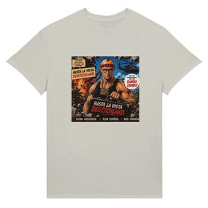 Puede incluir: Una camiseta gris claro con un estampado gráfico de una figura musculosa que lleva una cinta en la cabeza con la palabra FRITZ, gafas y una cadena de oro. El texto dice HASTA LA VISTA DEUTSCHLAND, WAS IST DUBATZ, RAMBO ZAMBO, KEINE AUSREDEN. KEIN ZURÜCK. NUR VORWÄR.