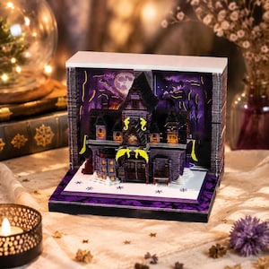 Puede incluir: Un diorama en miniatura de una casa encantada con una estructura de color morado oscuro y negro con ventanas amarillas brillantes. La escena incluye un fondo de luna llena, detalles arquitectónicos en capas y una base blanca decorada.