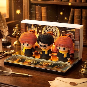 Puede incluir: Una caja de luz de papel recortado en 3D con tres figuras estilizadas de cabello naranja, negro y marrón rojizo, con bufandas amarillas y trajes negros. La base muestra el texto Magic World y el fondo presenta la silueta de un castillo.