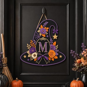 Pode incluir: Um enfeite de parede em forma de chapéu de bruxa roxo com uma moldura oval central contendo a letra M, decorado com flores de papel laranja e roxas, uma teia de aranha, uma estrela dourada e um laço preto e roxo, suspenso por uma corda.