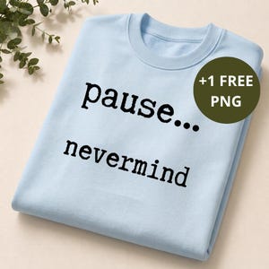 May include: A light blue crewneck sweatshirt featuring the black text "pause... nevermind" printed on the front. A dark olive green circular badge in the upper right corner contains the white text "+1 FREE PNG" to indicate a digital file inclusion.