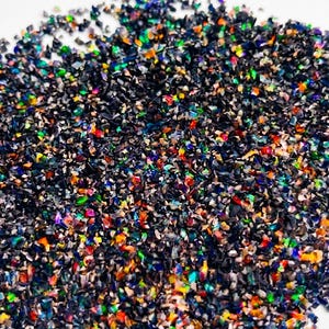 Könnte beinhalten: Eine Ansammlung kleiner, unregelmäßiger, zerkleinerter Opalfragmente mit einer tiefschwarzen Grundfarbe und lebendigen, mehrfarbigen, irisierenden Blitzen in Rot, Grün, Orange und Blau, die über die winzigen, gezackten Steinstücke verteilt sind.