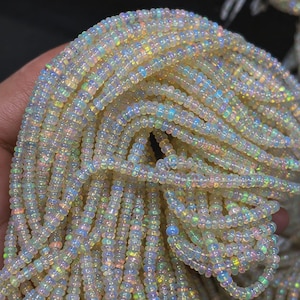 May include: A collection of small, round, translucent beads strung together on multiple threads. The beads are off-white and feature a distinct iridescent play-of-color, displaying flashes of blue, green, yellow, and pink light across their surfaces.
