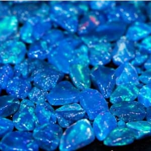 May include: A collection of small, tumbled blue opal stones with a vibrant, iridescent finish. Each stone features a polished, irregular shape with flashes of bright cyan, deep navy, and occasional hints of orange and yellow light reflections.