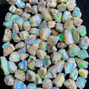 May include: A collection of raw, unpolished opal stones featuring a milky white base with iridescent flashes of blue, green, and orange. Each stone displays a unique, irregular shape with rough, textured surfaces and varying levels of translucency.