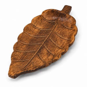 Puede incluir: Una bandeja de madera de color marrón oscuro tallada con forma de hoja. La bandeja presenta una nervadura central prominente y nervaduras laterales más pequeñas grabadas en la superficie, con un veteado texturizado y un pequeño tallo.