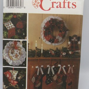 May include: A Simplicity Crafts sewing pattern envelope, number 9796, featuring instructions for holiday decorations. The cover displays a plaid wreath, four stockings with bows, a fabric star, a gingerbread ornament, and a small angel doll.
