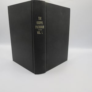 May include: A black hardcover book titled The Gospel Preacher Vol. I. The title is printed in gold lettering on the spine. The book is standing upright, showing the front cover and the spine, with a solid black matte finish on the cover material.