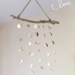 May include: A driftwood mobile with white seashells hanging from it. The mobile is suspended from the ceiling with twine. The word "love" is written in cursive on the wall behind the mobile.