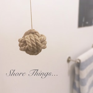 Op de afbeelding: Een close-up van een beige touw dat in een knoop is geknoopt en aan het plafond hangt. De tekst "Shore Things..." staat onder de knoop.