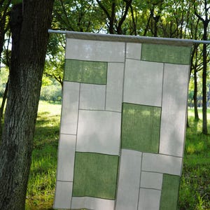 Op de afbeelding: Een rechthoekig stoffen paneel met een geometrisch patchworkontwerp van afwisselende witte en saliegroene blokken. Het textiel is geconstrueerd met zichtbare naden die de rechthoekige secties scheiden, wat een rasterachtig patroon creëert.