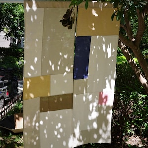 Könnte beinhalten: Ein rechteckiger Stoffvorhang mit einem Patchwork-Design aus verschiedenen einfarbigen Paneelen in Creme, Senfgelb, Marineblau, Olivgrün und einem kleinen blassrosa Quadrat. Das Textil besteht aus mehreren zusammengenähten Stoffsegmenten.