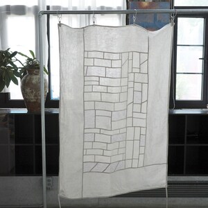 Peut inclure: Un panneau rectangulaire en tissu blanc présentant un motif géométrique central composé de fines lignes gris clair disposées en grille de briques. Le panneau est suspendu à une tige métallique par trois pinces argentées.