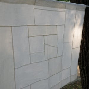 K&ouml;nnte beinhalten: Ein rechteckiges wei&szlig;es Stoffpaneel mit einem geometrischen Gittermuster aus feinen N&auml;hten. Das halbtransparente Textil zeigt eine Reihe von miteinander verbundenen Quadraten und Rechtecken unterschiedlicher Gr&ouml;&szlig;e, die ein strukturiertes, lineares Design bilden.