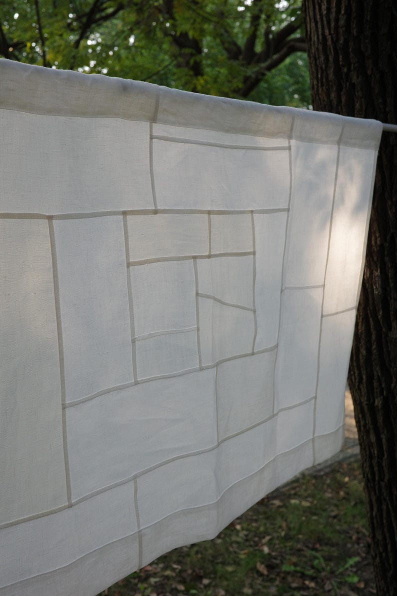 K&ouml;nnte beinhalten: Ein rechteckiges wei&szlig;es Stoffpaneel mit einem geometrischen Gittermuster aus feinen N&auml;hten. Das halbtransparente Textil zeigt eine Reihe von miteinander verbundenen Quadraten und Rechtecken unterschiedlicher Gr&ouml;&szlig;e, die ein strukturiertes, lineares Design bilden.