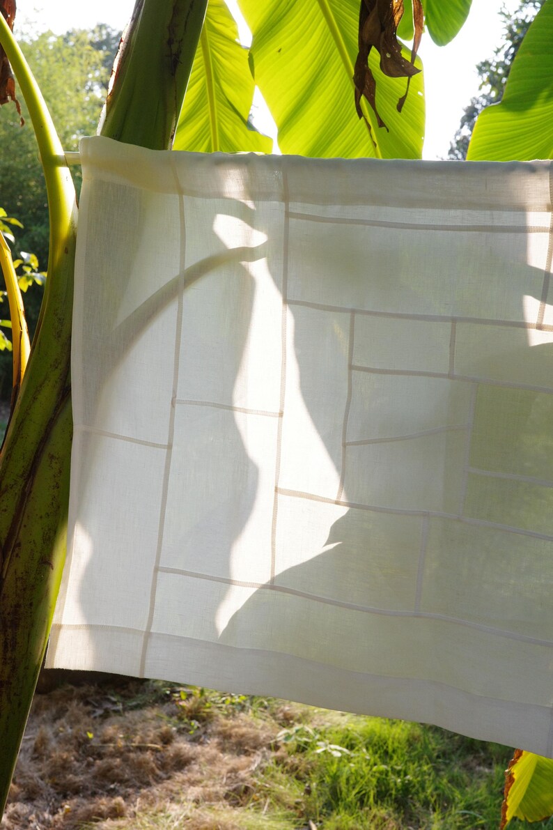 K&ouml;nnte beinhalten: Ein rechteckiges, cremewei&szlig;es Stoffpaneel mit einem geometrischen Gittermuster aus gen&auml;hten N&auml;hten. Das halbtransparente Textil zeigt eine Reihe verschiedener rechteckiger und quadratischer Abschnitte, die zu einer strukturierten, linearen Komposition zusammengef&uuml;gt sind.