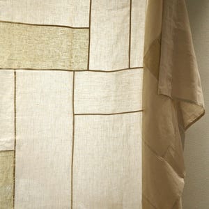 Puede incluir: Un panel de tela semitransparente con un dise&ntilde;o de patchwork de secciones rectangulares en varios tonos de blanco roto, crema y beige claro. Los segmentos est&aacute;n unidos por costuras lineales finas de color marr&oacute;n oscuro.