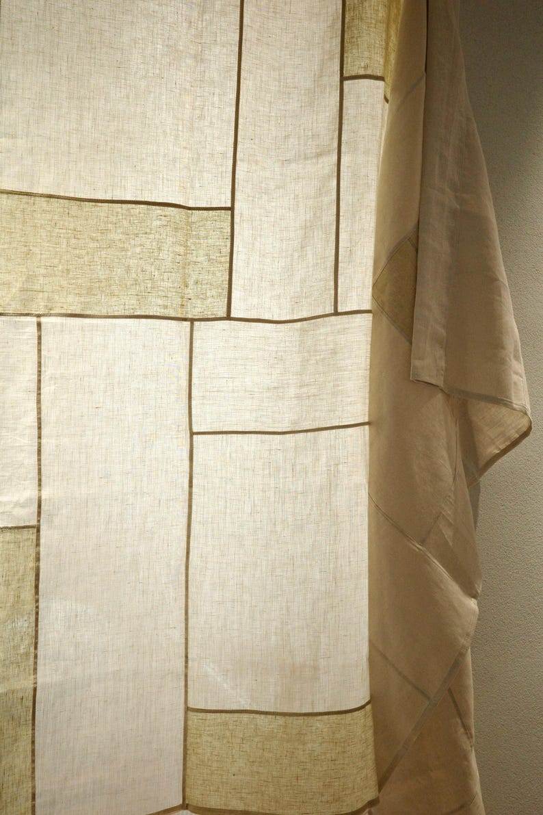 Puede incluir: Un panel de tela semitransparente con un dise&ntilde;o de patchwork de secciones rectangulares en varios tonos de blanco roto, crema y beige claro. Los segmentos est&aacute;n unidos por costuras lineales finas de color marr&oacute;n oscuro.