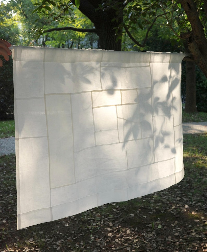 K&ouml;nnte beinhalten: Ein rechteckiges Paneel aus wei&szlig;em Stoff mit einem Patchwork-Design aus verschieden gro&szlig;en, zusammengen&auml;hten Rechtecken. Das halbtransparente Material weist ein sichtbares Raster aus N&auml;hten und einen Tunnelzug zur Aufh&auml;ngung auf.
