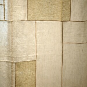 Puede incluir: Un panel de cortina con un dise&ntilde;o de patchwork de segmentos de tela rectangulares en varios tonos de beige y bronceado. La tela tiene una textura tejida visible, y cada secci&oacute;n rectangular est&aacute; separada por finas l&iacute;neas verticales y horizontales marrones.