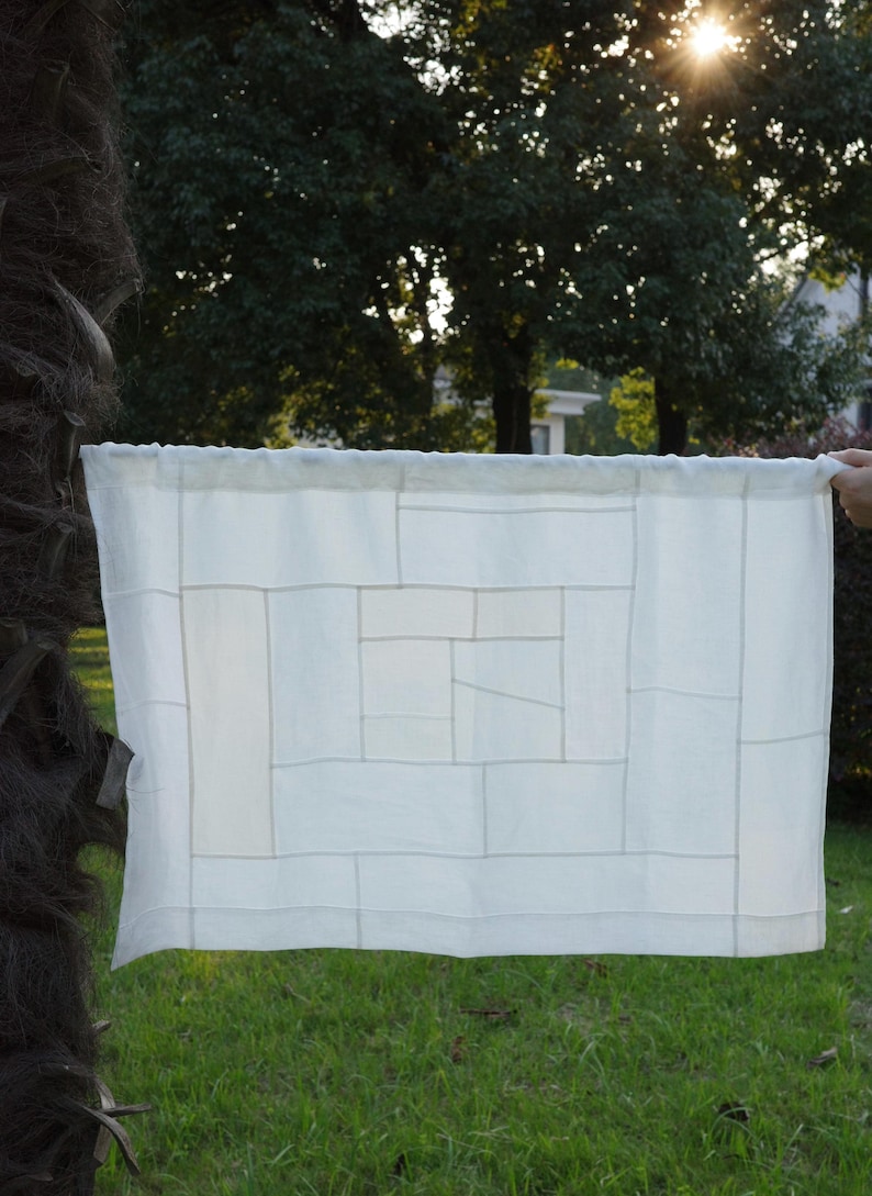 K&ouml;nnte beinhalten: Ein rechteckiges wei&szlig;es Stoffpaneel mit einem geometrischen Patchwork-Design, das aus verschieden gro&szlig;en rechteckigen und quadratischen Segmenten besteht, die mit feinen, sichtbaren N&auml;hten zu einem Gittermuster verbunden sind.