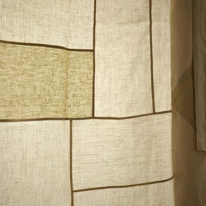Puede incluir: Un panel de cortina con un dise&ntilde;o de patchwork de secciones rectangulares de tela en color blanco roto y verde oliva claro. Los paneles est&aacute;n unidos por finas costuras lineales de color marr&oacute;n oscuro, creando un patr&oacute;n de cuadr&iacute;cula en el tejido.