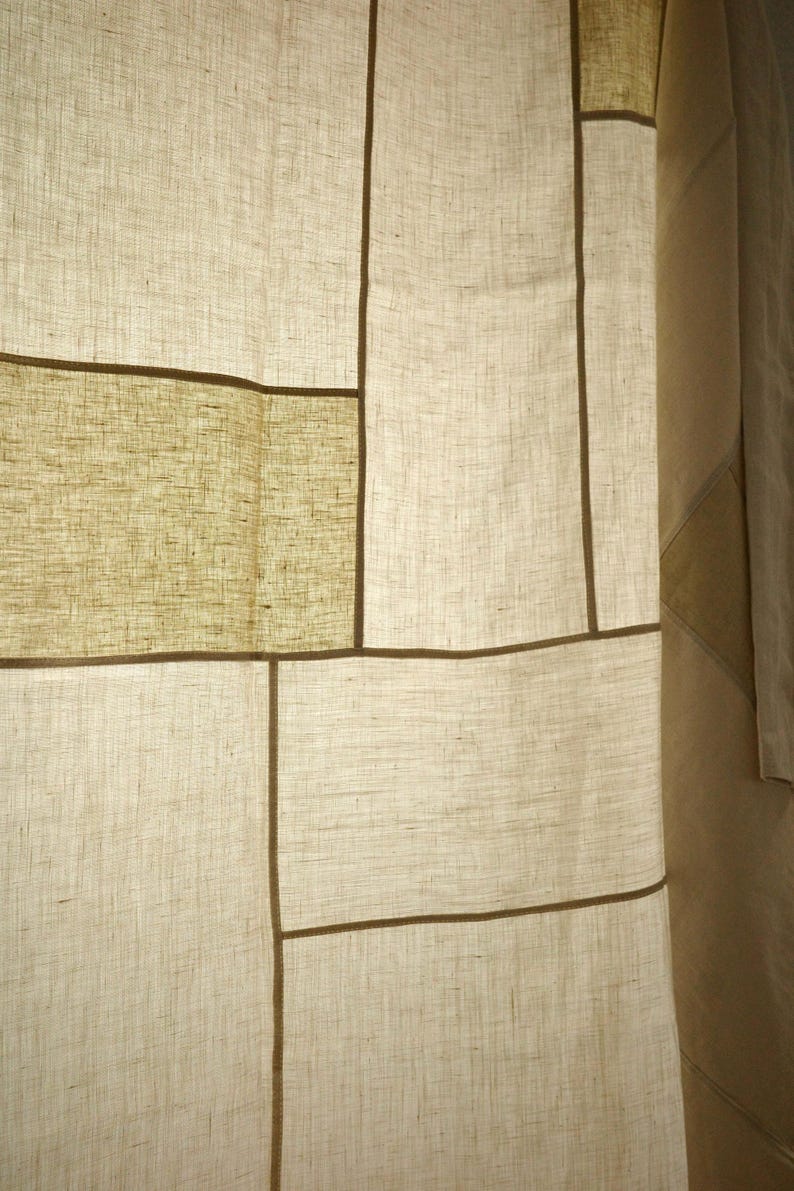 Puede incluir: Un panel de cortina con un dise&ntilde;o de patchwork de secciones rectangulares de tela en color blanco roto y verde oliva claro. Los paneles est&aacute;n unidos por finas costuras lineales de color marr&oacute;n oscuro, creando un patr&oacute;n de cuadr&iacute;cula en el tejido.