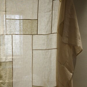 Puede incluir: Un panel de cortina semitransparente con un dise&ntilde;o de patchwork de segmentos rectangulares en varios tonos de beige, crema y bronceado claro. La tela tiene una textura tejida visible y los segmentos est&aacute;n unidos por finas costuras lineales de color marr&oacute;n oscuro.
