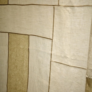 Puede incluir: Un panel textil con un dise&ntilde;o de patchwork de segmentos rectangulares en varios tonos de beige y bronceado. La tela tiene una textura tejida visible y cada secci&oacute;n est&aacute; unida por costuras finas de color marr&oacute;n oscuro que crean un patr&oacute;n de rejilla.