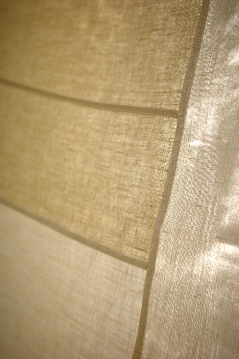 Puede incluir: Una cortina de tela semitransparente con una textura tejida visible en tonos beige claro y bronceado. El material presenta paneles horizontales unidos por costuras finas y rectas, permitiendo que la luz pase a trav&eacute;s del tejido fibroso y transl&uacute;cido.