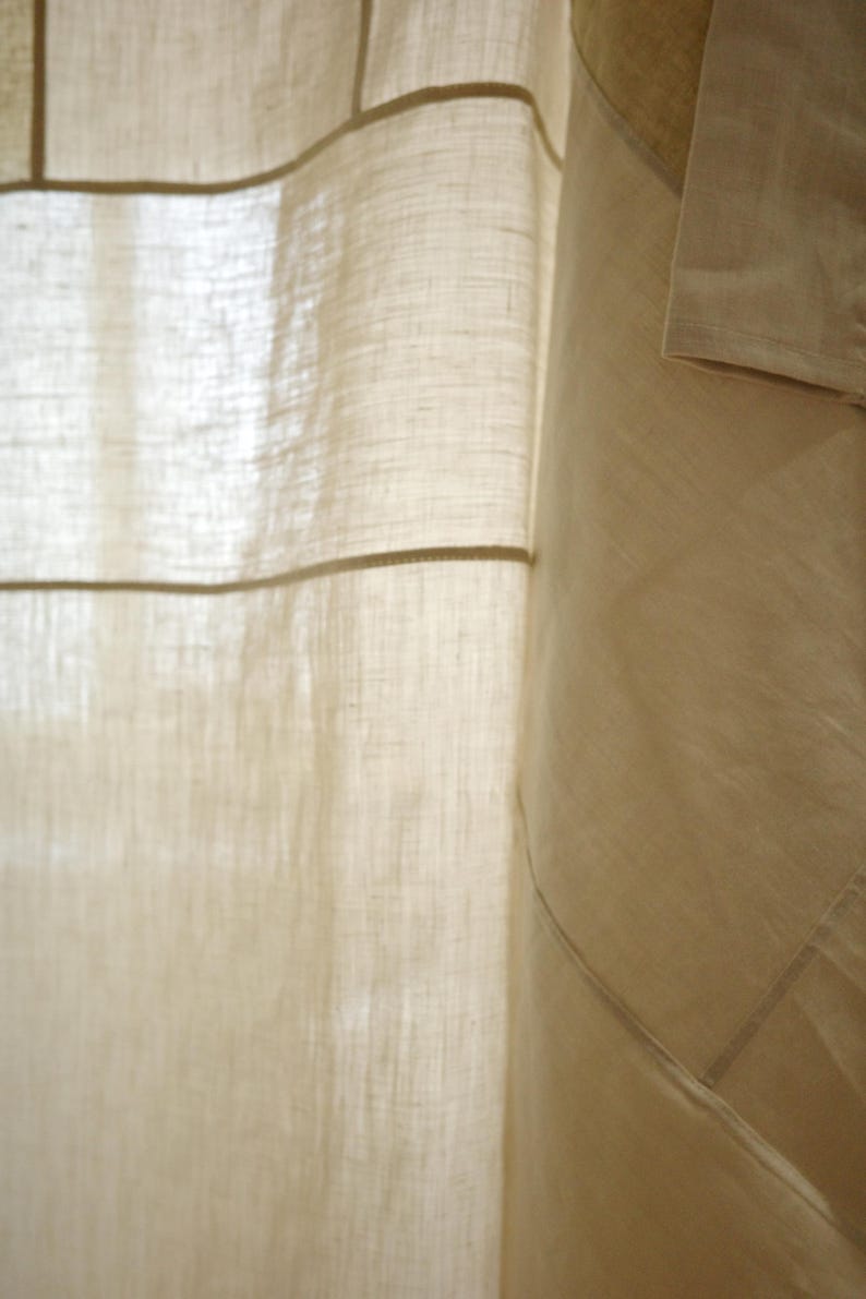 Puede incluir: Una cortina de color beige hecha de una tela semitransparente y texturizada con un tejido visible. La cortina presenta un patr&oacute;n de cuadr&iacute;cula creado por costuras horizontales y verticales, con un panel beige s&oacute;lido m&aacute;s oscuro a la derecha.