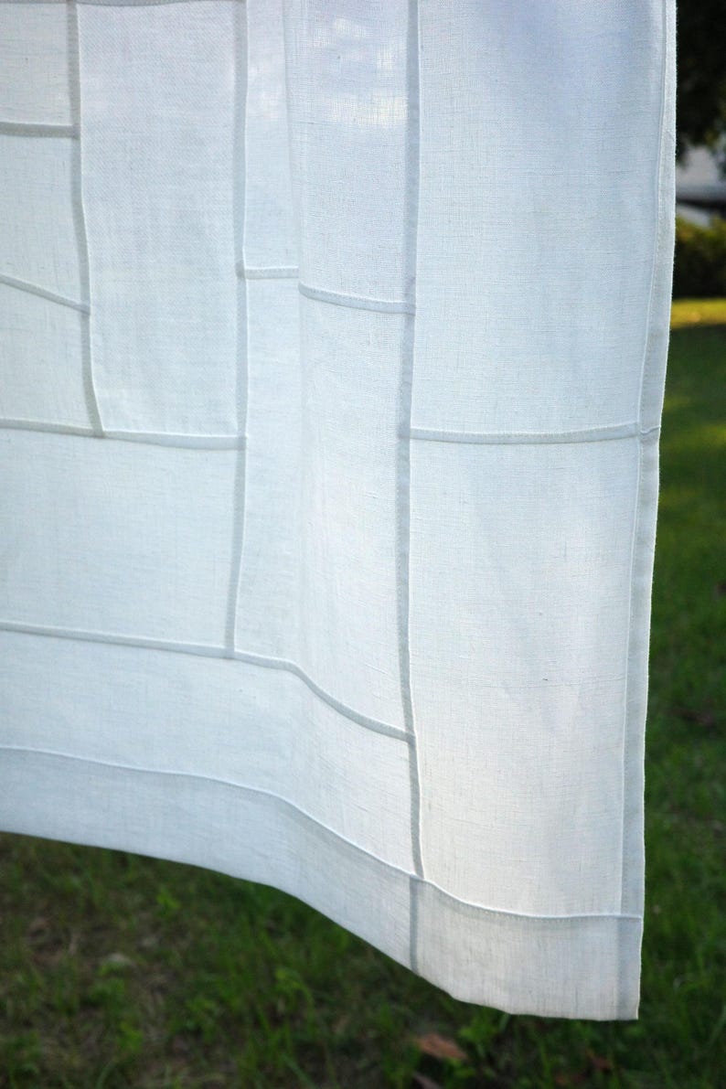 K&ouml;nnte beinhalten: Ein wei&szlig;er Vorhang aus halbtransparentem Stoff mit einem gitterartigen Muster aus vertikalen und horizontalen N&auml;hten. Das helle Textil weist eine sichtbare Webstruktur auf und wird vom Sonnenlicht beleuchtet, was weiche Schatten an den N&auml;hten erzeugt.