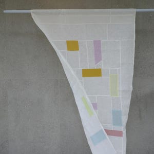 May include: A white rectangular textile hanging from a horizontal rod, featuring a grid of thin white lines and scattered solid-colored geometric rectangles in shades of mustard yellow, pale lavender, light green, soft blue, and muted rose pink.