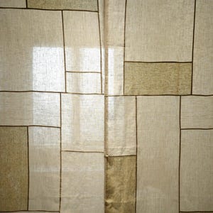 Puede incluir: Un panel de cortina semitransparente con un patr&oacute;n geom&eacute;trico de l&iacute;neas de color marr&oacute;n oscuro que se cruzan sobre una tela texturizada de color beige claro. El dise&ntilde;o consta de varias formas rectangulares de diferentes tama&ntilde;os, creando una apariencia de cuadr&iacute;cula.