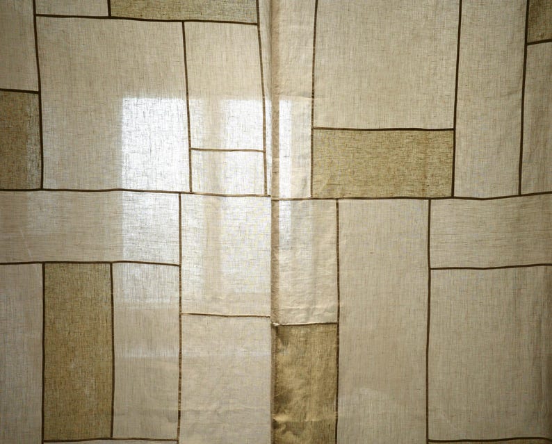 Puede incluir: Un panel de cortina semitransparente con un patr&oacute;n geom&eacute;trico de l&iacute;neas de color marr&oacute;n oscuro que se cruzan sobre una tela texturizada de color beige claro. El dise&ntilde;o consta de varias formas rectangulares de diferentes tama&ntilde;os, creando una apariencia de cuadr&iacute;cula.