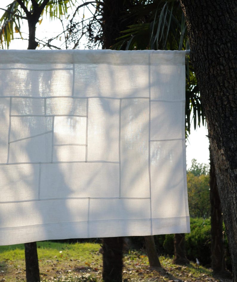 K&ouml;nnte beinhalten: Ein wei&szlig;es, rechteckiges Stoffpaneel mit einem Patchwork-Design aus verschieden gro&szlig;en Rechtecken und Quadraten. Das halbtransparente Material ist mit sichtbaren N&auml;hten zusammengesetzt, die die einzelnen Teile verbinden und ein Gittermuster bilden.