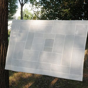 K&ouml;nnte beinhalten: Ein rechteckiges wei&szlig;es Stoffpaneel mit einem geometrischen Patchwork-Design aus verschieden gro&szlig;en rechteckigen Segmenten. Das halbtransparente Material weist ein gitterartiges Muster aus gen&auml;hten N&auml;hten auf.