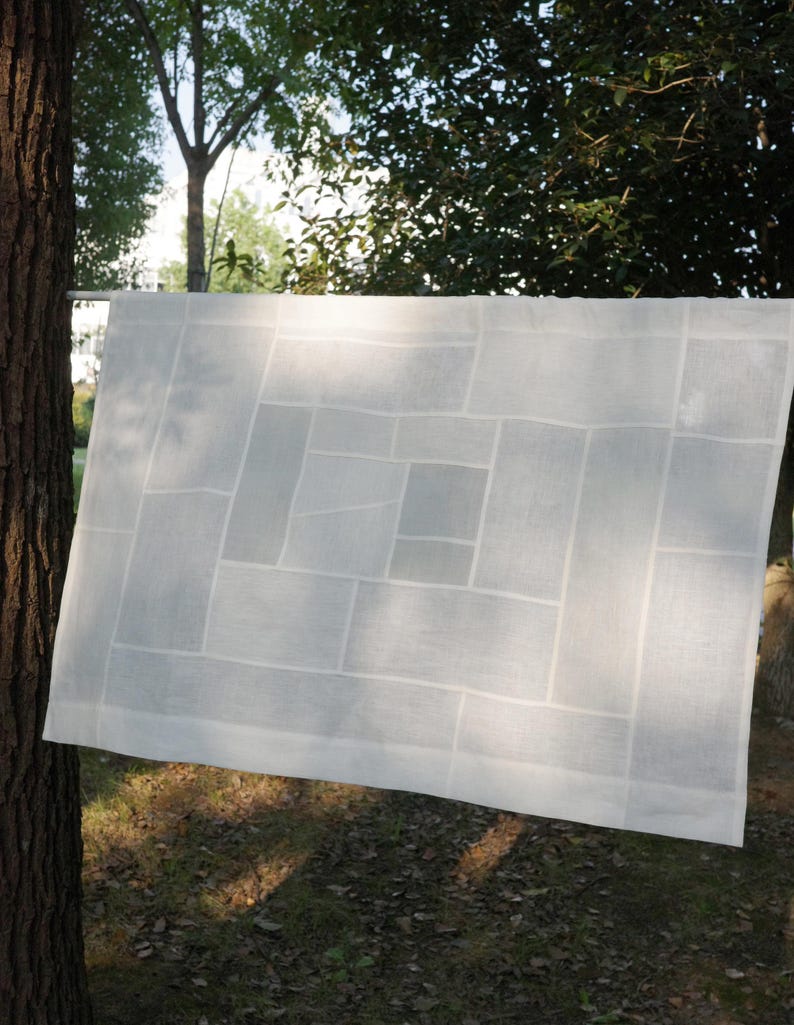 K&ouml;nnte beinhalten: Ein rechteckiges wei&szlig;es Stoffpaneel mit einem geometrischen Patchwork-Design aus verschieden gro&szlig;en rechteckigen Segmenten. Das halbtransparente Material weist ein gitterartiges Muster aus gen&auml;hten N&auml;hten auf.