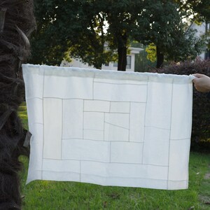 K&ouml;nnte beinhalten: Ein rechteckiger, cremewei&szlig;er Stoffvorhang mit einem geometrischen Patchwork-Design, das aus verschiedenen zusammengen&auml;hten rechteckigen Paneelen besteht. Der Stoff hat einen Stangendurchzug an der Oberkante und wirkt halbtransparent mit sichtbaren N&auml;hten.