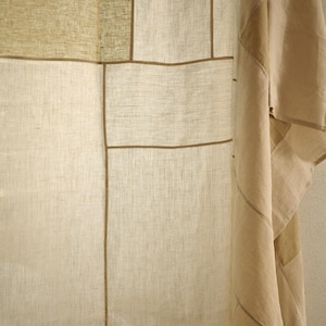 Puede incluir: Una cortina de color beige y bronceado claro con un dise&ntilde;o de patchwork tipo cuadr&iacute;cula y textura de tela visible. El panel est&aacute; construido con secciones rectangulares de material tipo lino separadas por ribetes lineales marr&oacute;n oscuro.